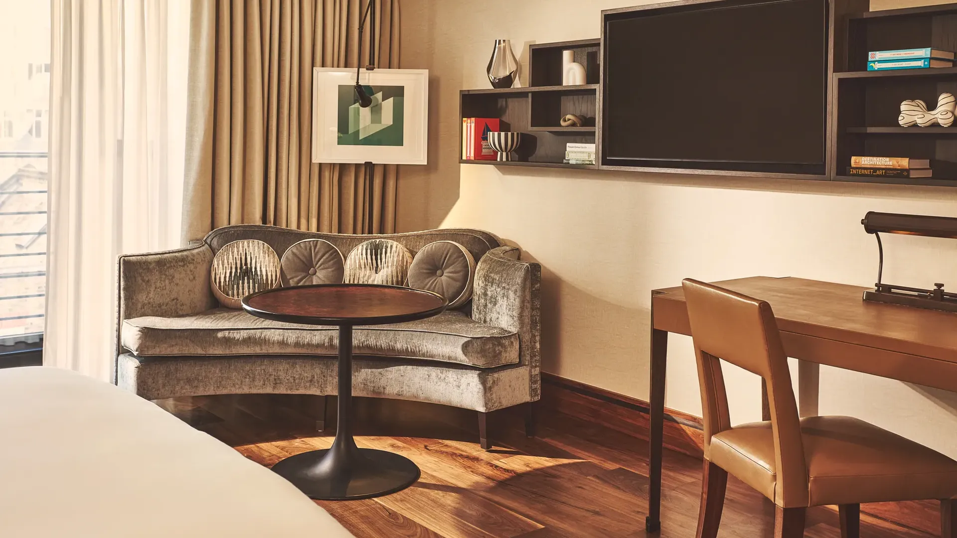 Cozy room corner with a curved sofa, round table, wall-mounted shelves, and large TV beside floor-to-ceiling curtains.