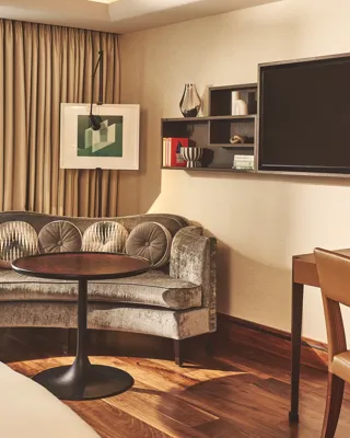 Cozy room corner with a curved sofa, round table, wall-mounted shelves, and large TV beside floor-to-ceiling curtains.
