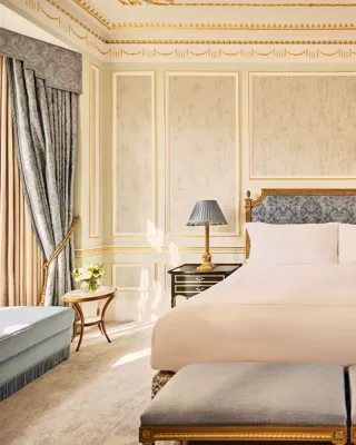 King-size bed with upholstered headboard in a classically styled bedroom featuring gold detailing, blue accents, and twin benches at the foot of the bed.