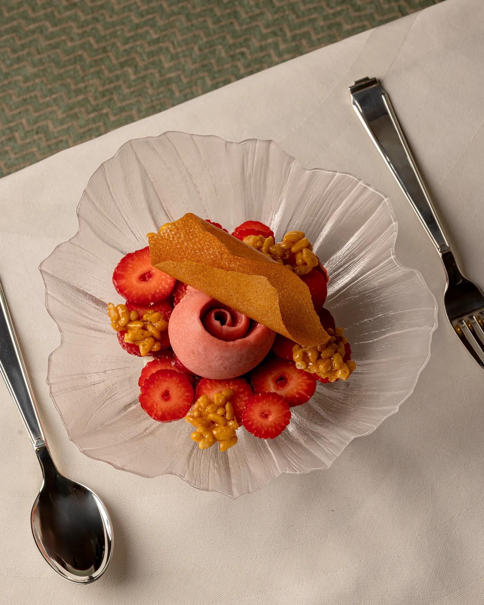 Strawberry dessert with pink sorbet, sliced strawberries and caramelised clusters on a glass plate.