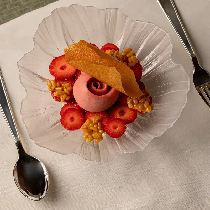 Strawberry dessert with pink sorbet, sliced strawberries and caramelised clusters on a glass plate.