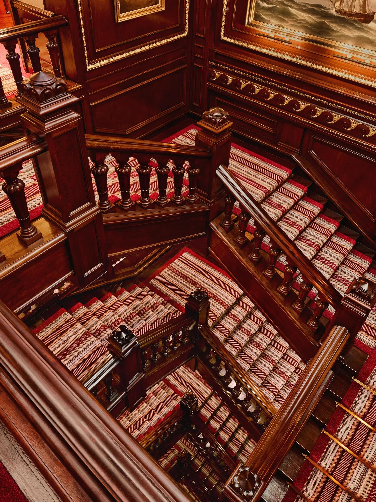 Grand wooden staircase with carved banisters and red striped carpet.