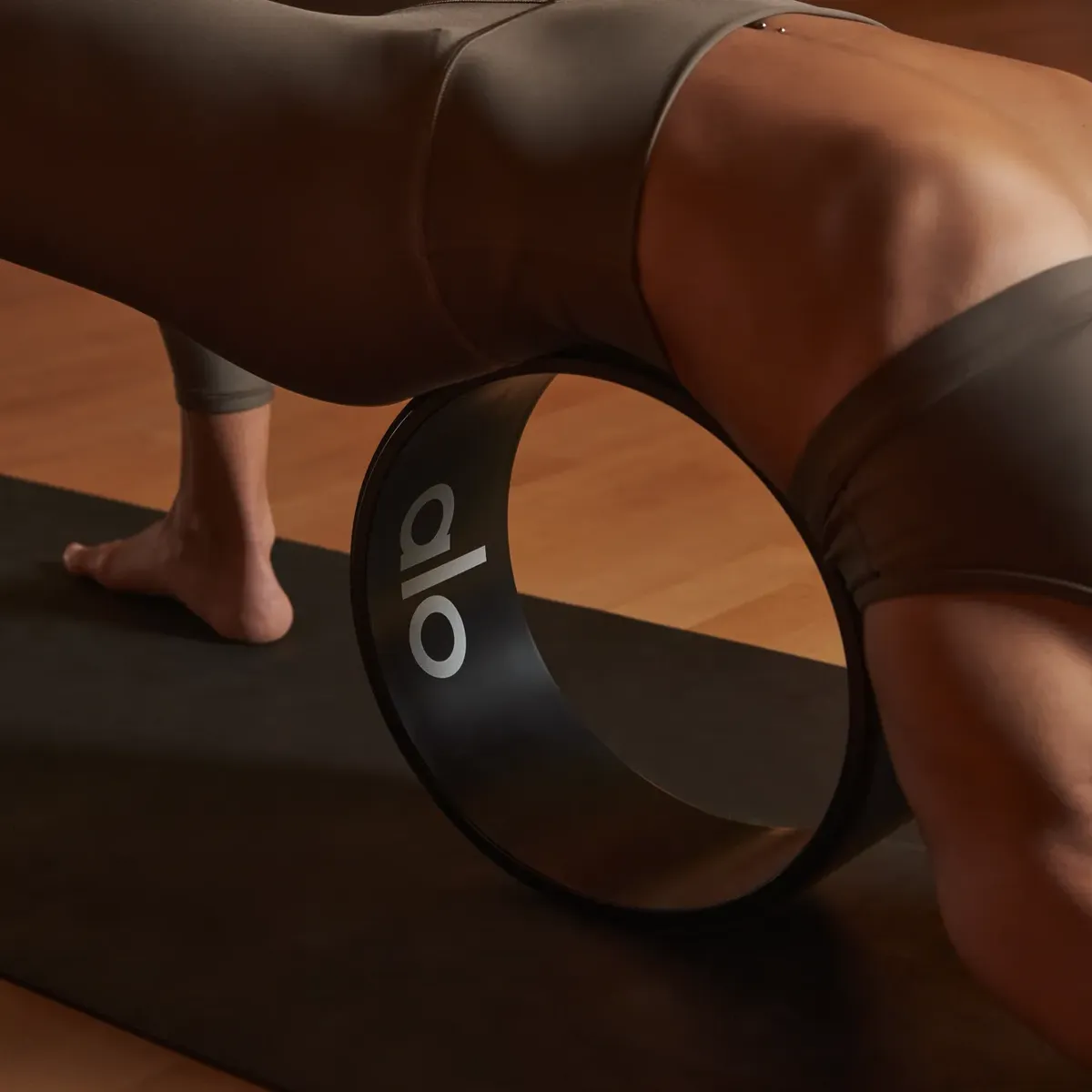 Person using a yoga wheel on a mat, performing a strength and flexibility pose in a studio setting.