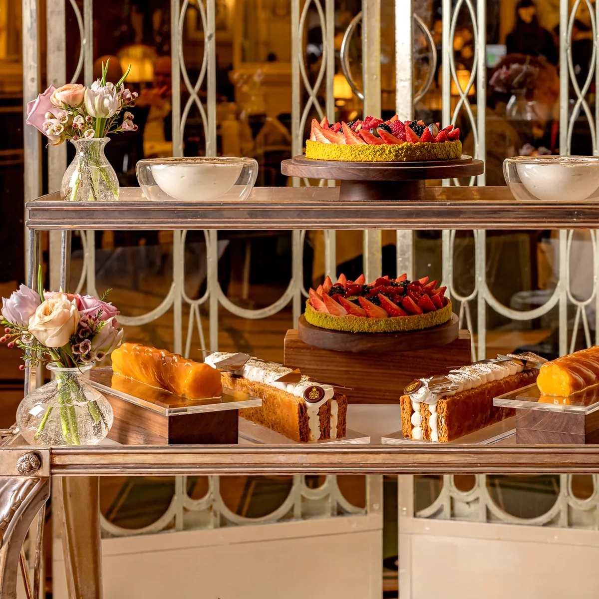 Two-tier dessert trolley with strawberry tarts, pastries and cakes, styled with small floral arrangements in an elegant dining room.