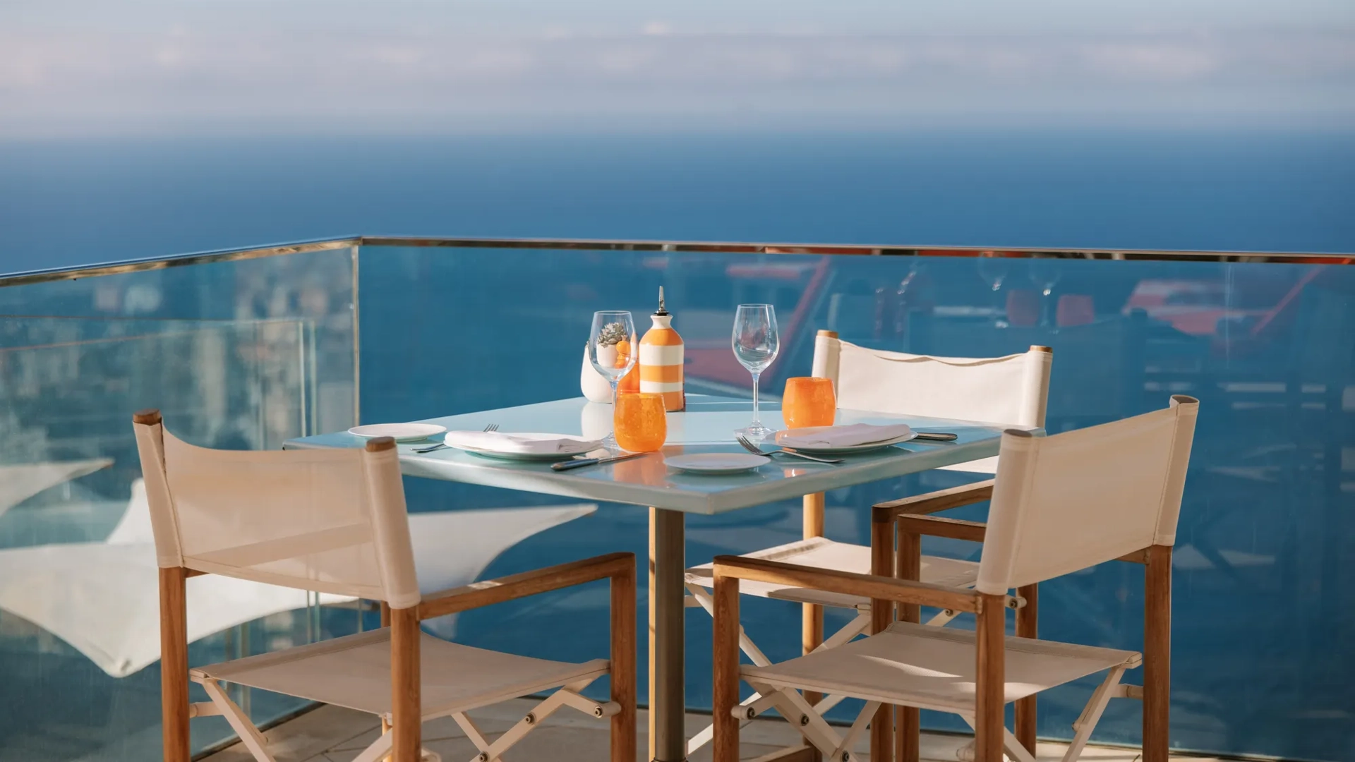 Table de terrasse en bord de mer dressée pour deux avec chaises blanches et vue sur l’océan.