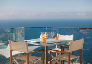 Table de terrasse en bord de mer dressée pour deux avec chaises blanches et vue sur l’océan.