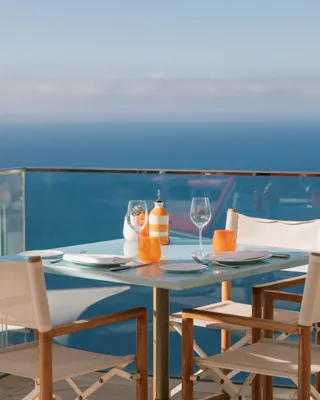 Table de terrasse en bord de mer dressée pour deux avec chaises blanches et vue sur l’océan.
