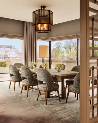 Elegant dining area with six upholstered chairs, wooden table, and large windows overlooking terrace with potted plants.