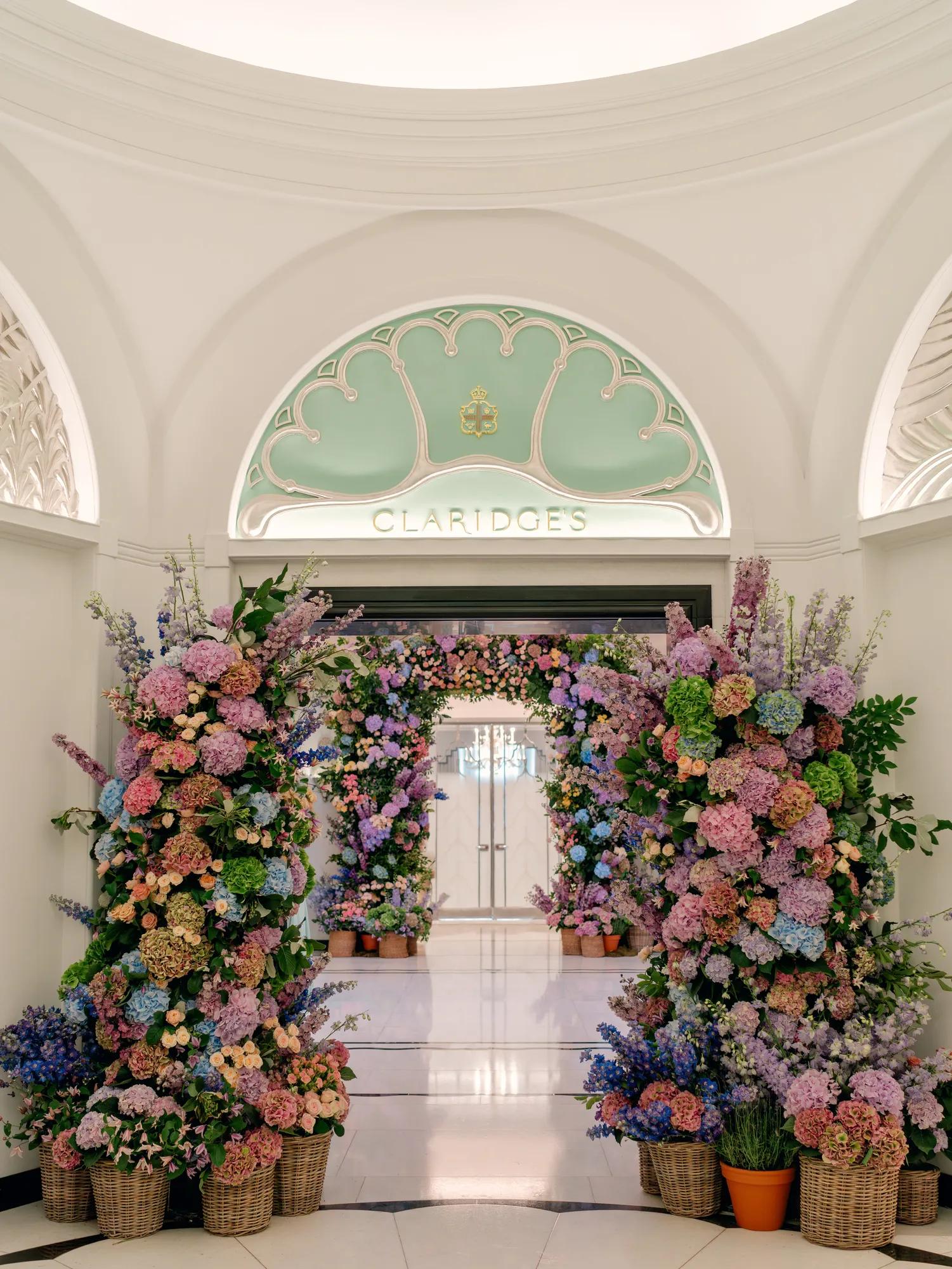 Floral arch of pink, purple and blue blooms frames the Claridge’s entrance beneath an arched ceiling.