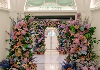 Floral arch of pink, purple and blue blooms frames the Claridge’s entrance beneath an arched ceiling.