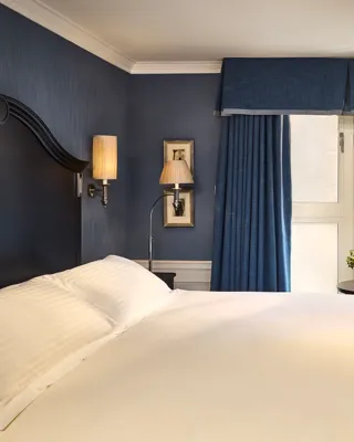 Elegant guest room with king bed, blue walls, armchair by window, and dressing table.