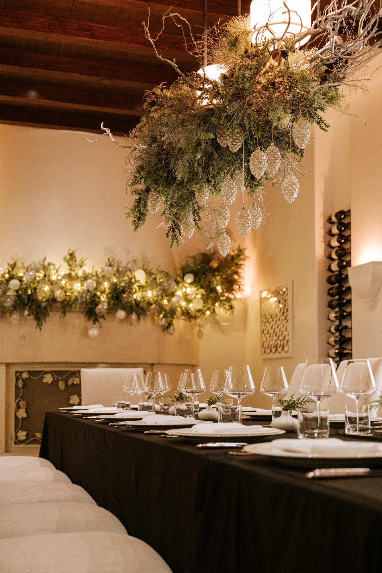Elegant private dining room with festive greenery, glowing garlands, hanging pinecone décor, and a beautifully set table for a holiday gathering.