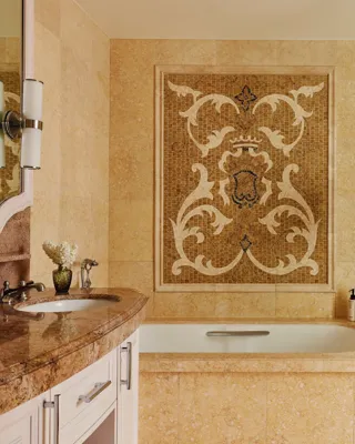 Elegant bath showing an ornate mosaic panel above the tub, stone vanity, and a glass‑enclosed walk‑in shower with chrome fixtures; limestone tile throughout.