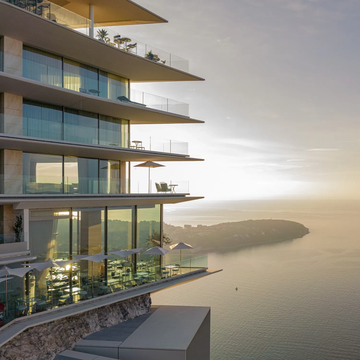 Modern cliffside hotel with glass balconies overlooking the sea at sunset.