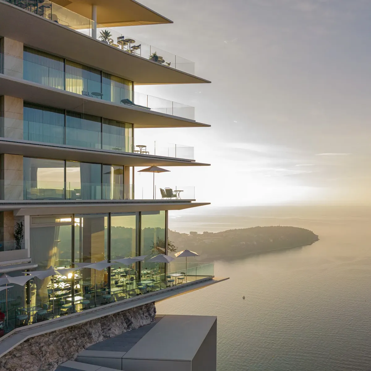 Modern cliffside hotel with glass balconies overlooking the sea at sunset.