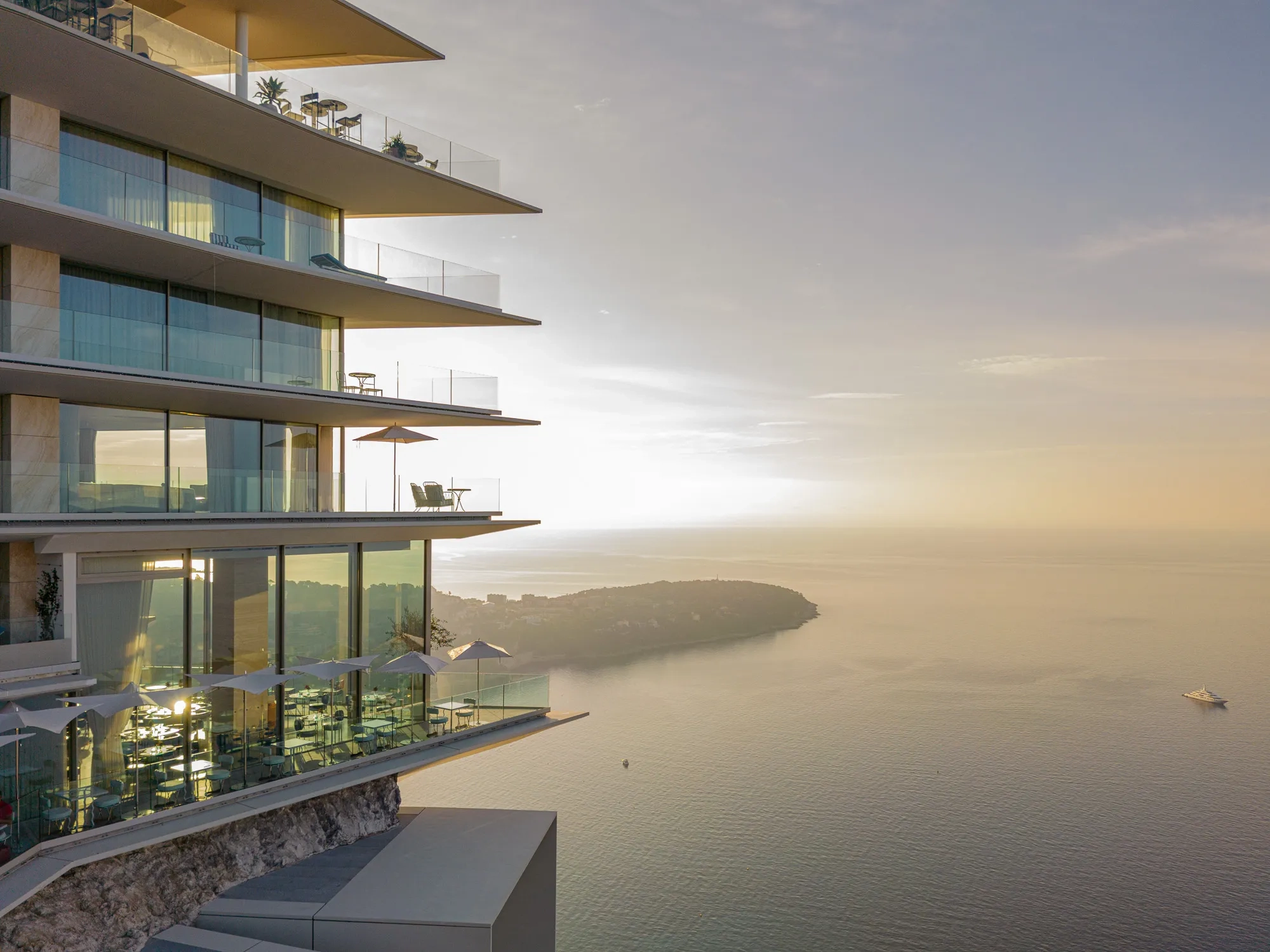 Modern cliffside hotel with glass balconies overlooking the sea at sunset.