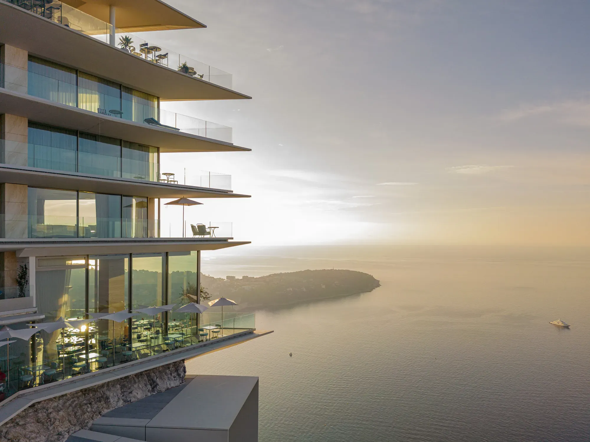 Modern cliffside hotel with glass balconies overlooking the sea at sunset.