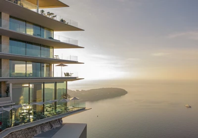 Modern cliffside hotel with glass balconies overlooking the sea at sunset.