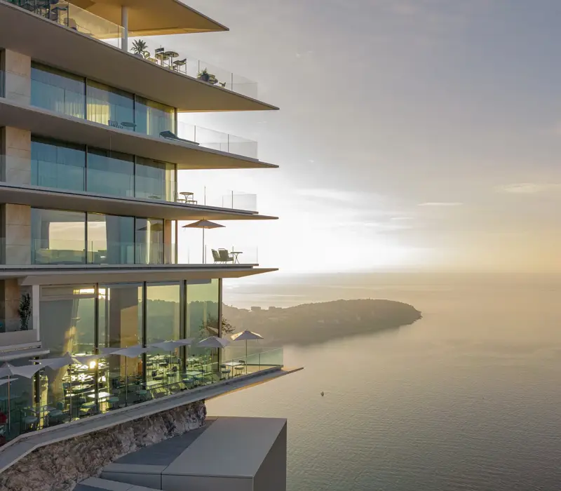 Modern cliffside hotel with glass balconies overlooking the sea at sunset.