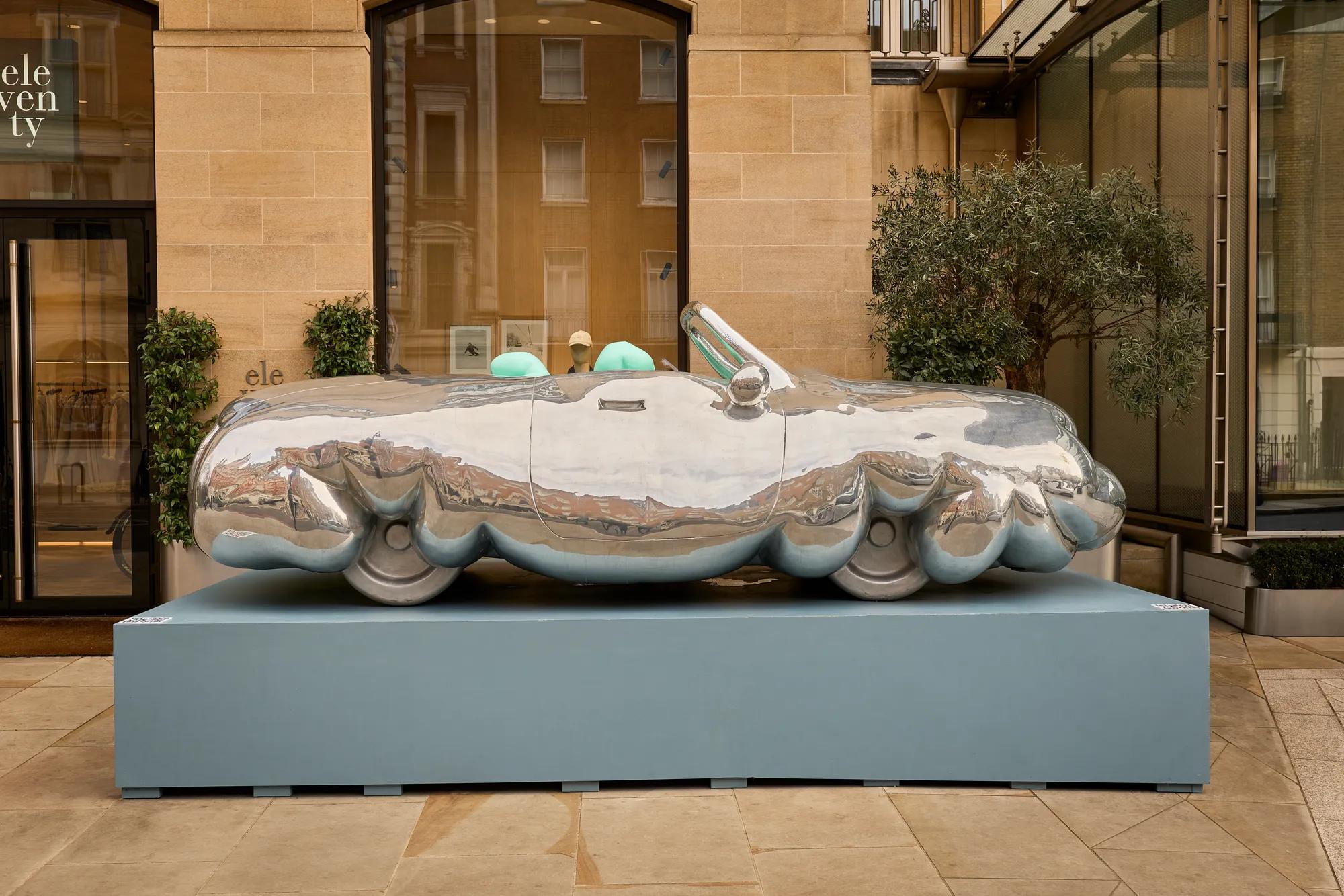 Reflective sculptural car on a plinth, with mirrored chrome body and turquoise seats.