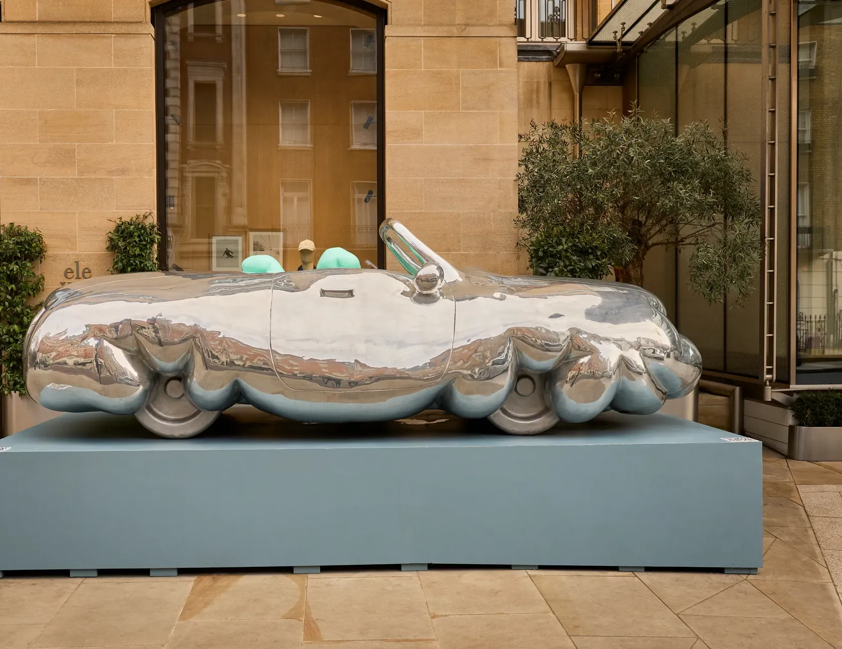 Reflective sculptural car on a plinth, with mirrored chrome body and turquoise seats.
