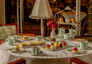 Afternoon tea table with pastries, sandwiches, striped teacups, and red floral centerpiece.