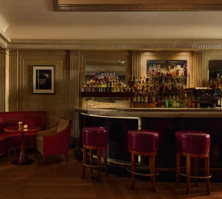 Elegant hotel bar with red leather seating, marble counter, and backlit spirits display.