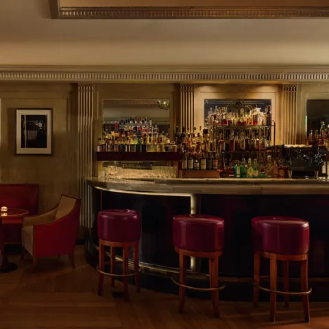 Elegant hotel bar with red leather seating, marble counter, and backlit spirits display.