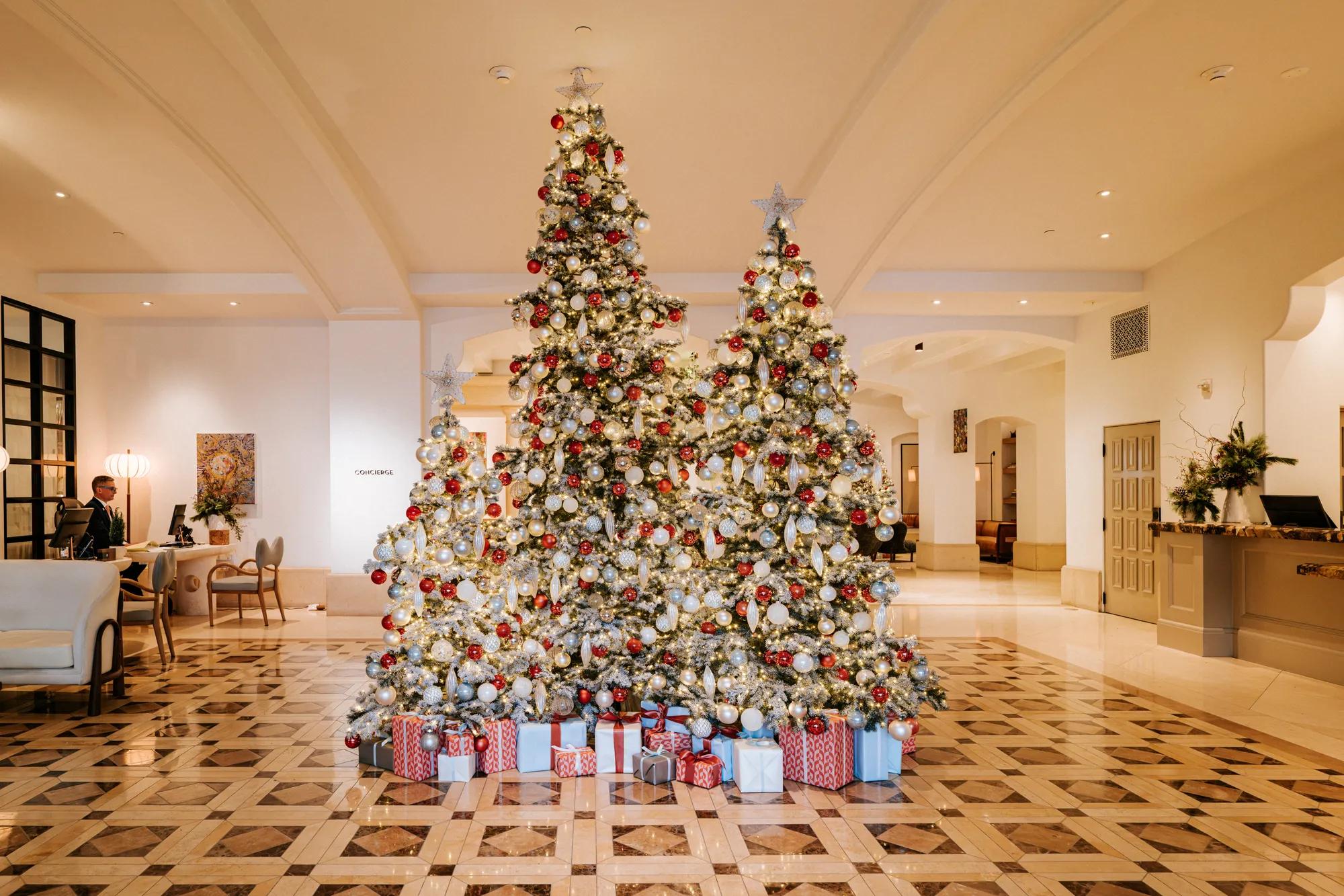 The Maybourne Beverly Hills entrance adorned with illuminated holiday trees, festive décor, wrapped gifts, and a decorated Christmas display.