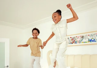 Two children holding hands, jumping on a hotel bed in a light-filled Hollywood suite