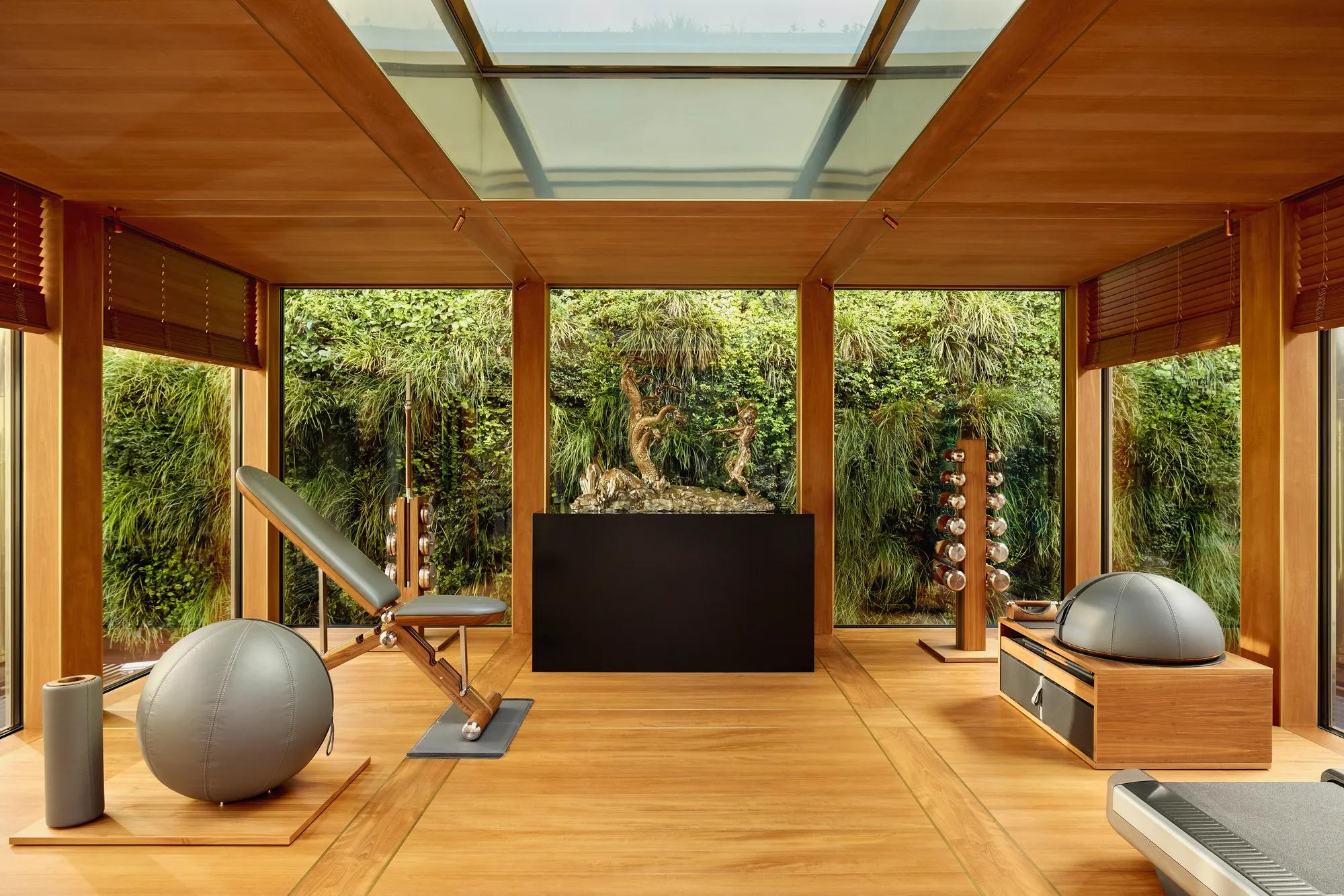 Private fitness room at Claridge’s with wood interiors, gym equipment, and floor-to-ceiling windows overlooking a green wall.