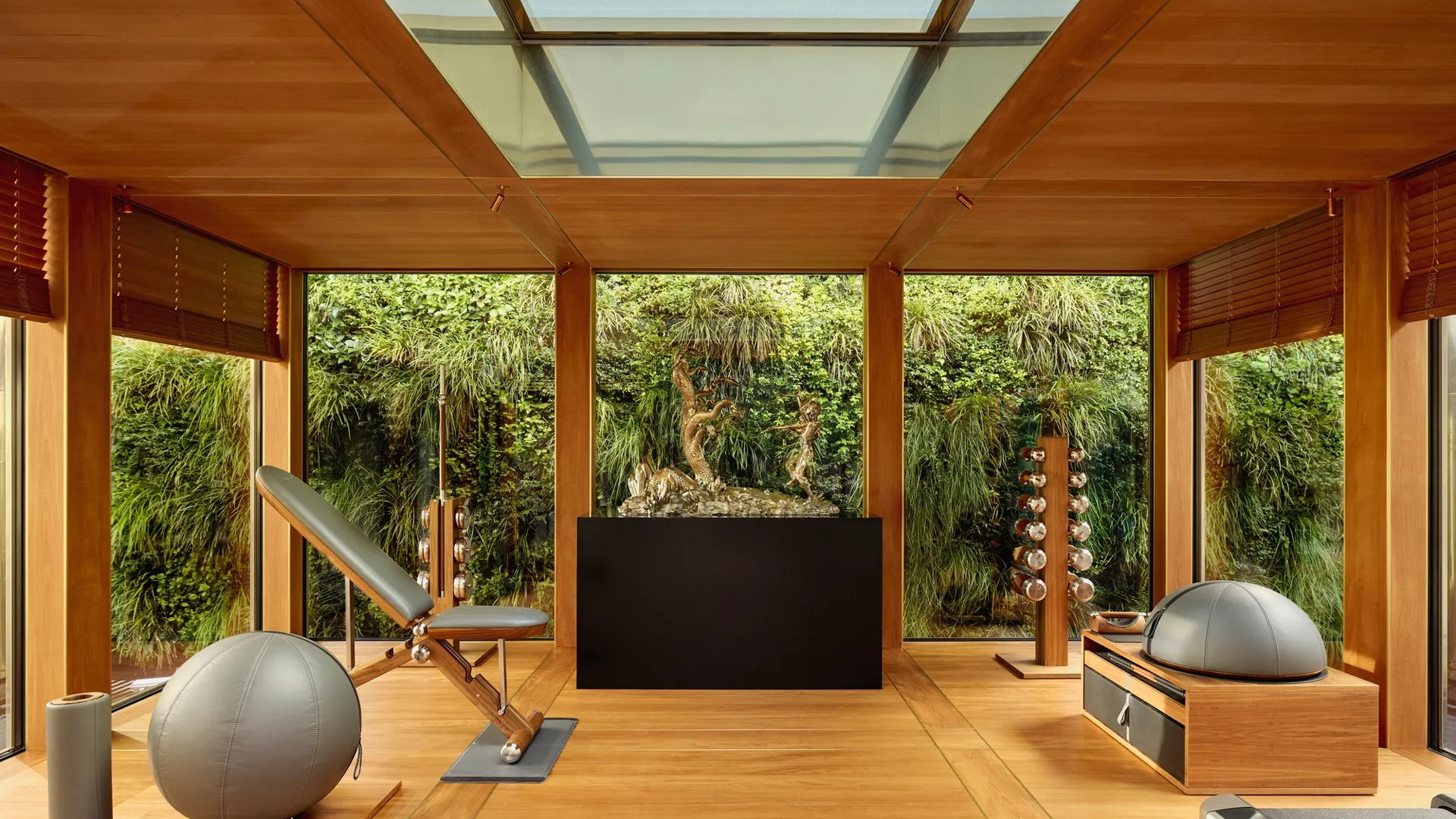 Private fitness room at Claridge’s with wood interiors, gym equipment, and floor-to-ceiling windows overlooking a green wall.