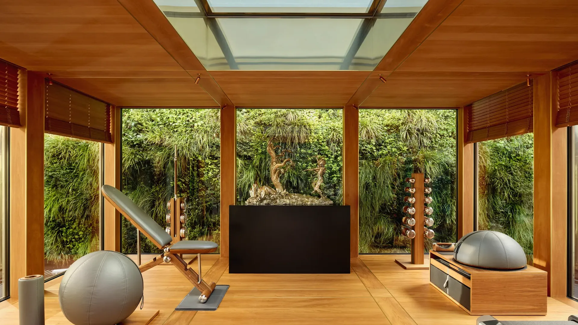 Private fitness room at Claridge’s with wood interiors, gym equipment, and floor-to-ceiling windows overlooking a green wall.