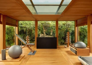 Private fitness room at Claridge’s with wood interiors, gym equipment, and floor-to-ceiling windows overlooking a green wall.