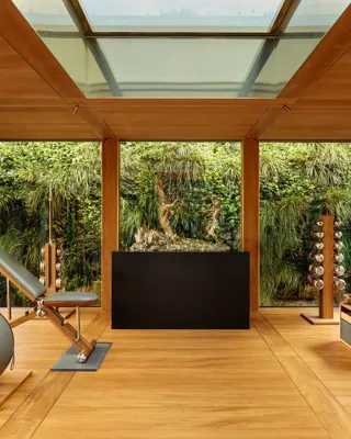 Private fitness room at Claridge’s with wood interiors, gym equipment, and floor-to-ceiling windows overlooking a green wall.