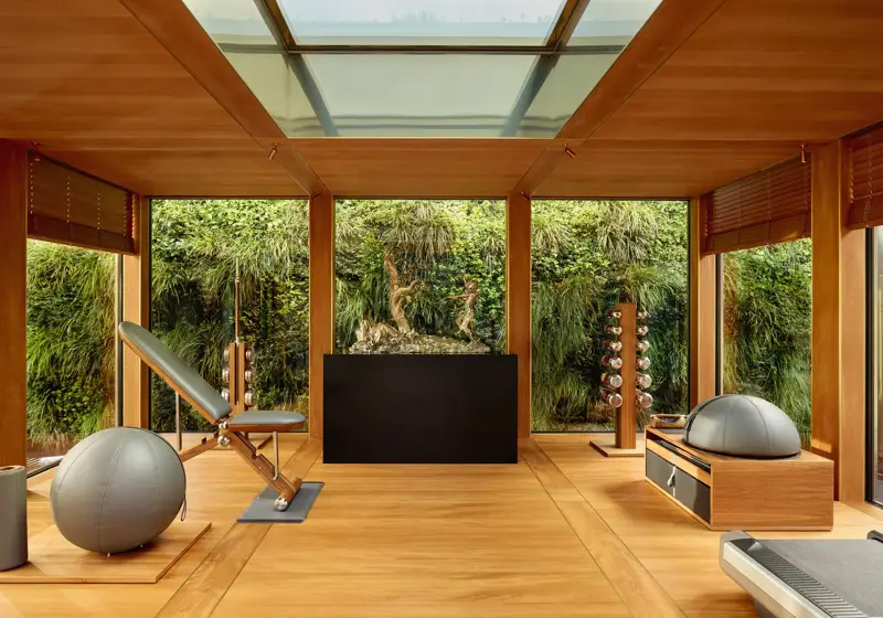 Private fitness room at Claridge’s with wood interiors, gym equipment, and floor-to-ceiling windows overlooking a green wall.