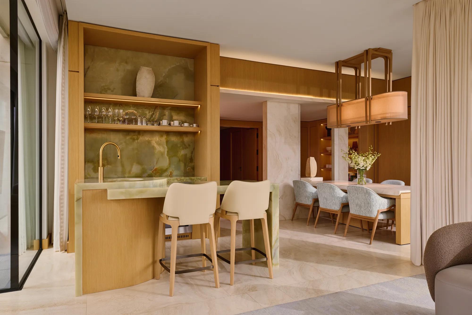 Elegant bar area with green onyx counter, high chairs, and open shelving leading to dining space with six upholstered chairs.