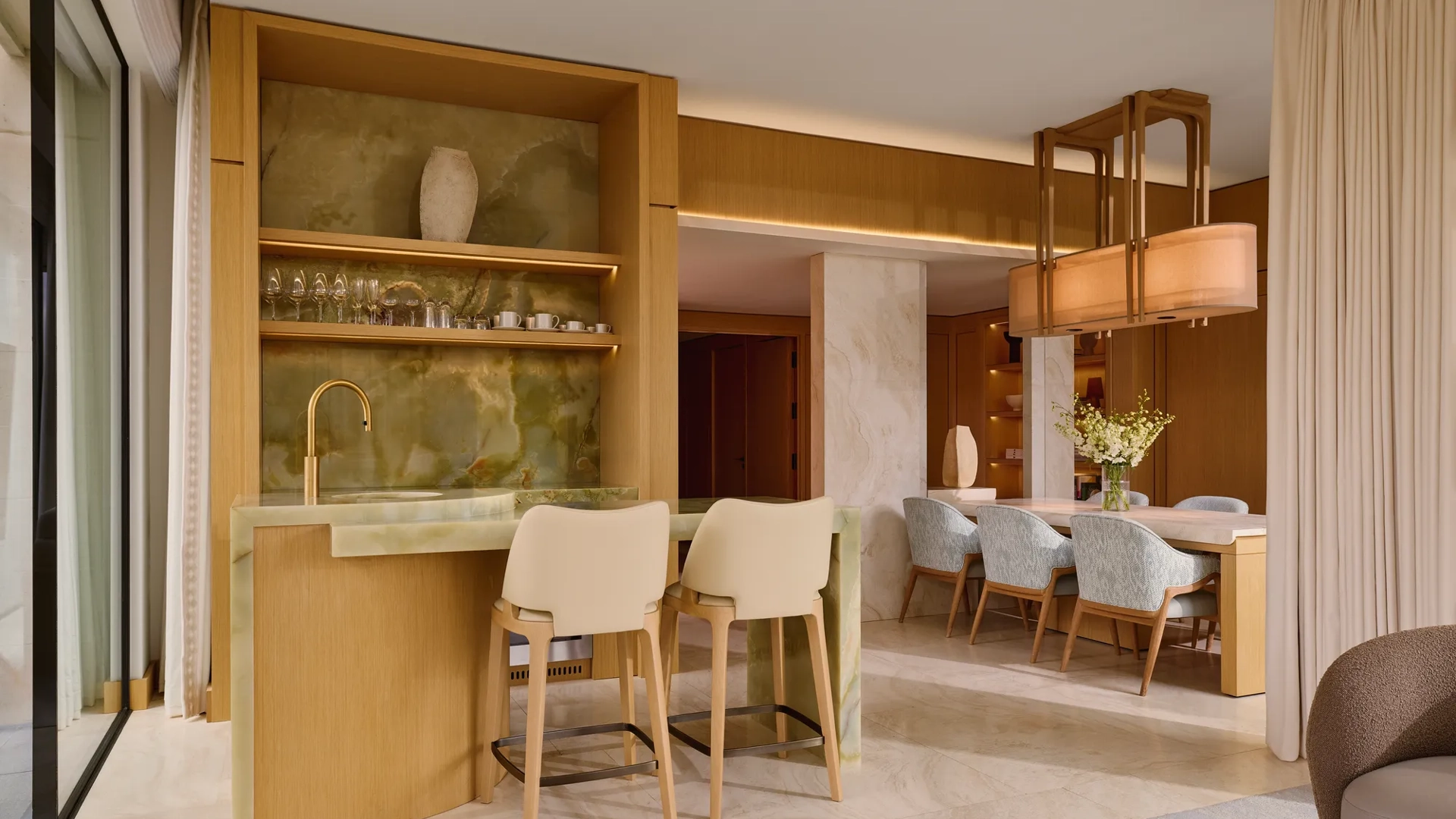 Elegant bar area with green onyx counter, high chairs, and open shelving leading to dining space with six upholstered chairs.