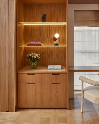 Wood-paneled workspace with built-in shelving and drawers, small desk by window, upholstered chair, and decorative lighting.