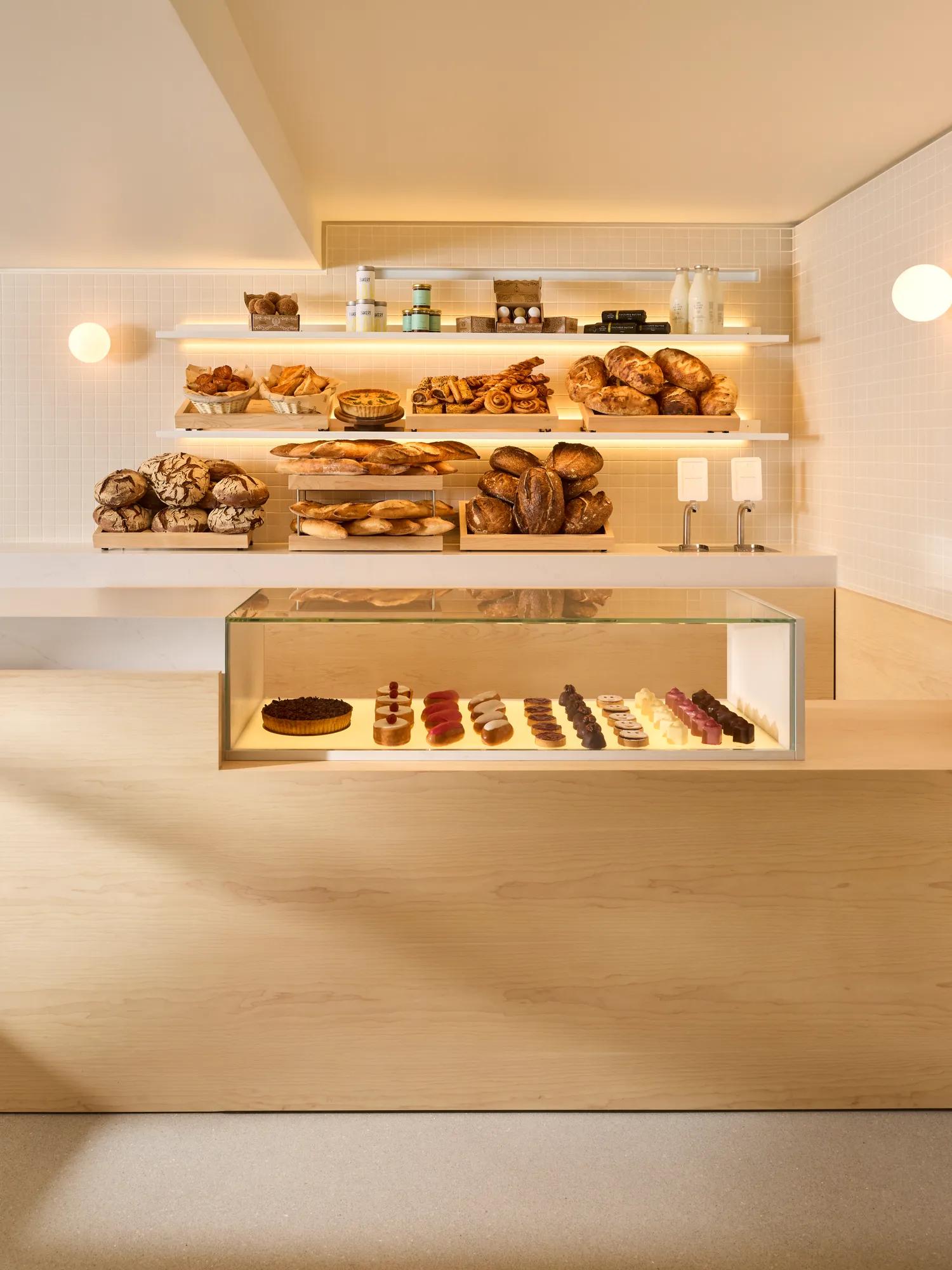 Modern bakery counter with shelves of artisan breads and pastries above a glass display of small desserts.