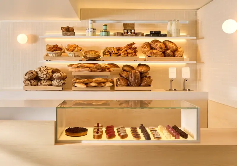 Modern bakery counter with shelves of artisan breads and pastries above a glass display of small desserts.