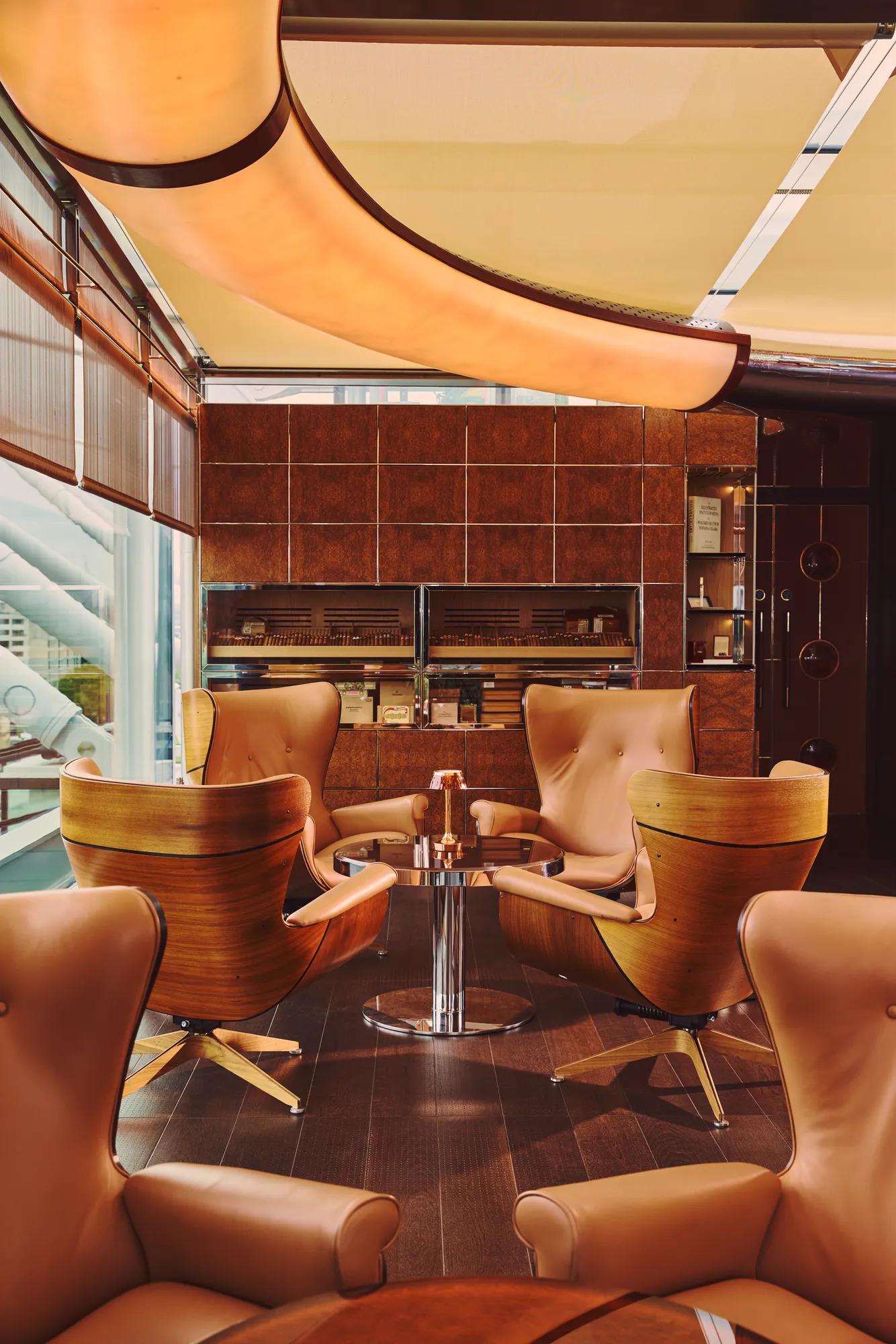 Intimate lounge seating with leather armchairs, round table and warm wood and tile interior beside large windows.