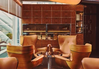 Intimate lounge seating with leather armchairs, round table and warm wood and tile interior beside large windows.
