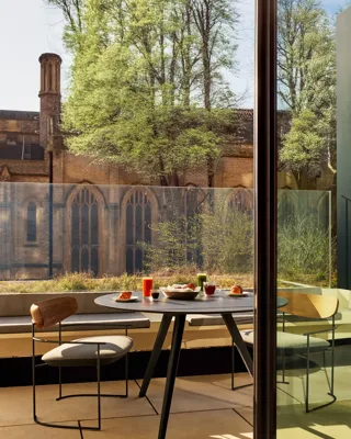 Outdoor table with croissants, juice, and coffee overlooking historic stone church and greenery.