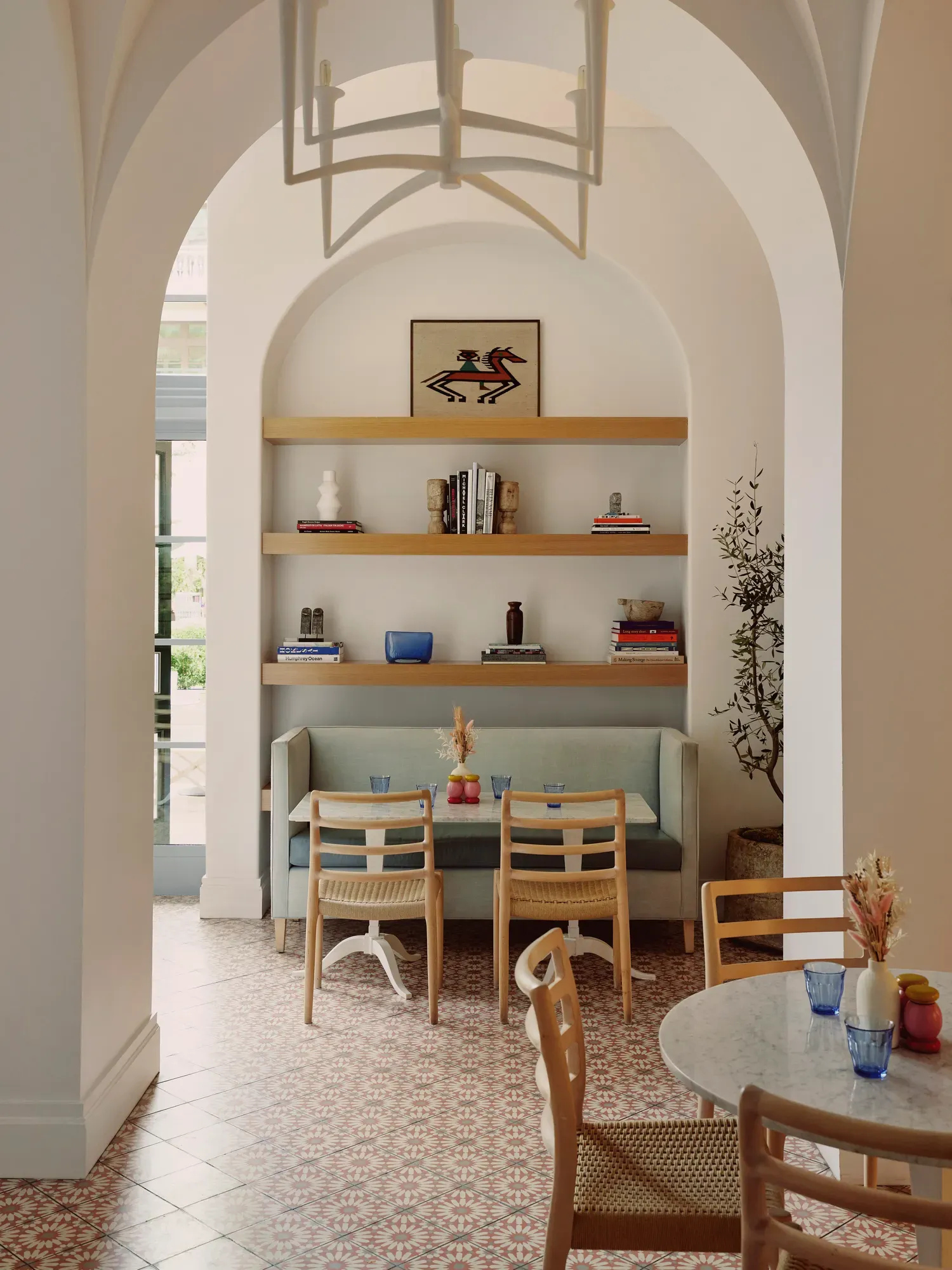 Café alcove with booth, two chairs, and shelves holding books, art, and vases beneath a vaulted arch.