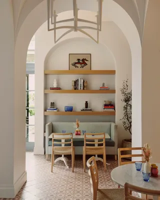 Café alcove with booth, two chairs, and shelves holding books, art, and vases beneath a vaulted arch.