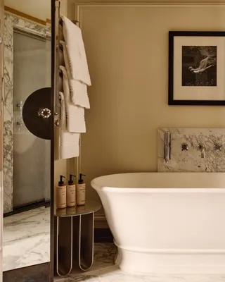 Elegant bathroom featuring a freestanding white bathtub with marble accents, a framed black-and-white photograph above, and soft lighting that highlights the cream walls and wood cabinetry.