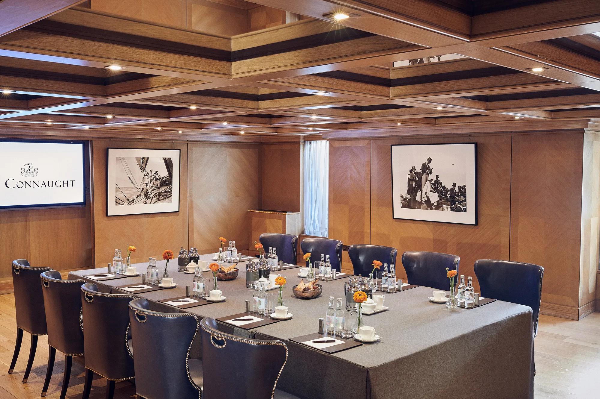 Wood-panelled meeting room with navy chairs around a square table set with water bottles and notepads.