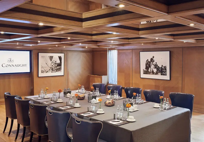 Wood-panelled meeting room with navy chairs around a square table set with water bottles and notepads.