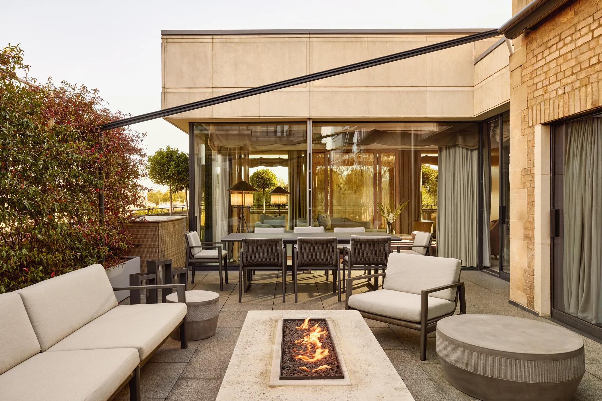 Penthouse terrace with modern fire pit, outdoor seating, and dining area beside large glass doors